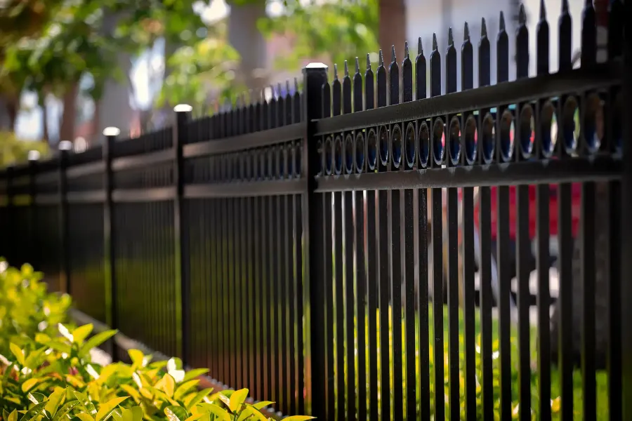 Black ornamental metal picket fence with pointed finials along a hedge